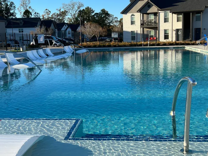 Luxurious apartment complex pool with modern lounge chairs, surrounded by elegant buildings and serene landscaping.