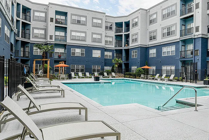 Inviting apartment complex courtyard featuring a large swimming pool, comfortable lounge chairs, and vibrant patio umbrellas.
