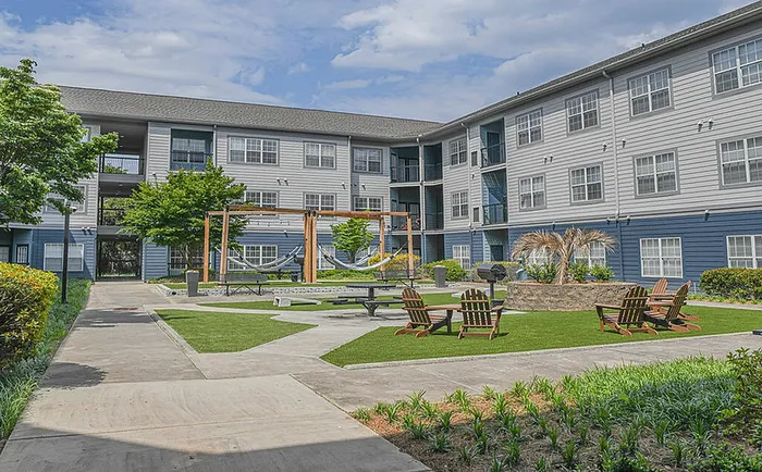 Modern apartment complex featuring vibrant courtyard with lush greenery, relaxing hammocks, and inviting outdoor seating area.