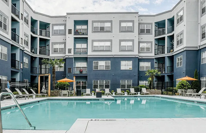Modern apartment complex with a luxurious outdoor pool, surrounded by stylish balconies and vibrant sun umbrellas.