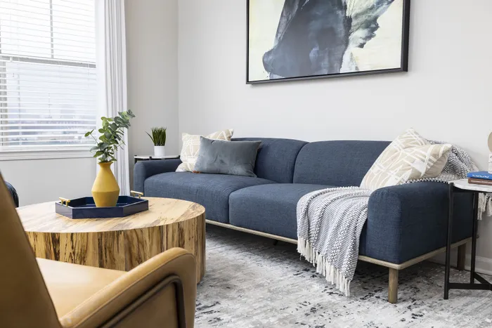 Chic living room with a modern blue sofa, elegant wooden coffee table, and artistic wall decor, creating an inviting and stylish atmosphere.