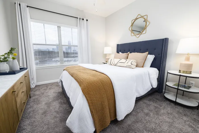 Chic bedroom featuring a plush blue headboard, elegant neutral bedding, and a stylish geometric mirror.