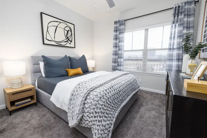 Elegant bedroom with modern decor, featuring a cozy grey bed, stylish abstract art, and abundant natural light.