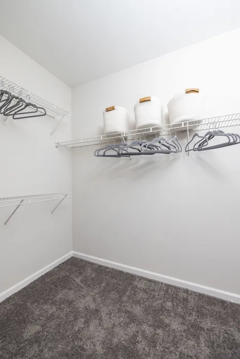 Spacious walk-in closet with sleek wire shelving, elegant gray carpet, and stylish white storage baskets.
