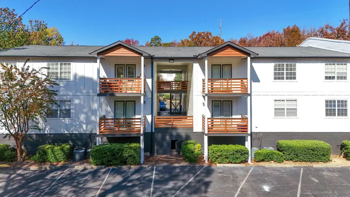 Charming apartment building with modern wooden balconies, surrounded by autumn trees and lush greenery, under a clear blue sky.