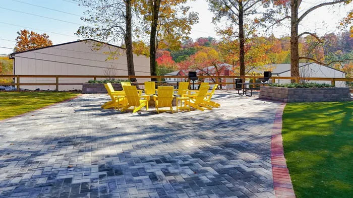 Charming outdoor patio with vibrant yellow chairs and a fire pit, surrounded by lush greenery and autumnal trees.