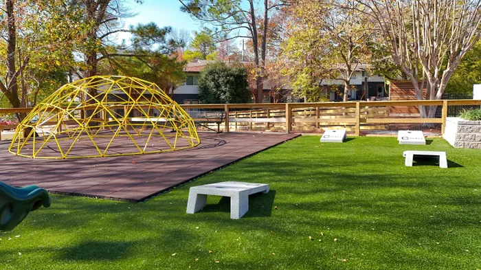 Inviting outdoor playground with a vibrant yellow climbing dome, lush artificial grass, and shaded seating area, perfect for family fun.