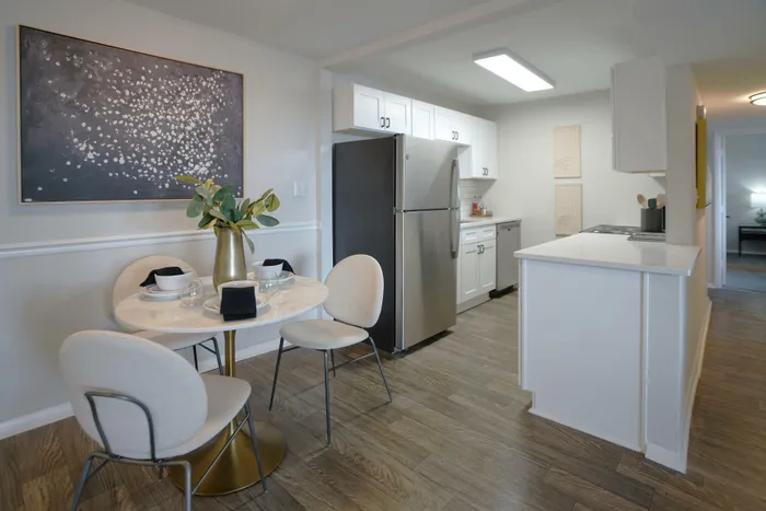 Modern kitchen and dining area with elegant decor, featuring a stainless steel fridge, chic wall art, and a cozy dining table set for three.