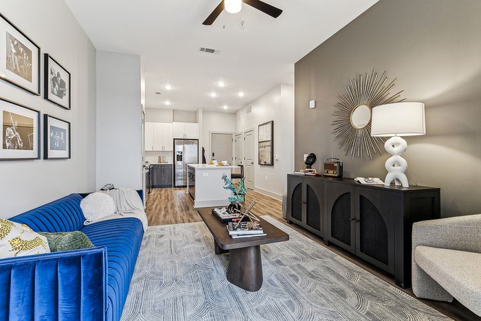 Chic modern living room with elegant blue sofa, stylish coffee table, and sleek open kitchen in the background, bathed in natural light.