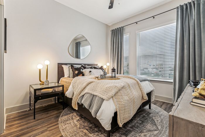 Cozy bedroom with modern decor featuring a plush bed, stylish bedside table lamps, and large windows with elegant curtains.