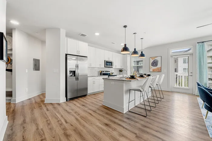 Modern kitchen with sleek stainless steel appliances, elegant white cabinetry, and a spacious island with stylish pendant lighting. Cozy breakfast bar features comfortable seating, enhancing the open-concept layout with luxurious hardwood flooring and ample natural light.
