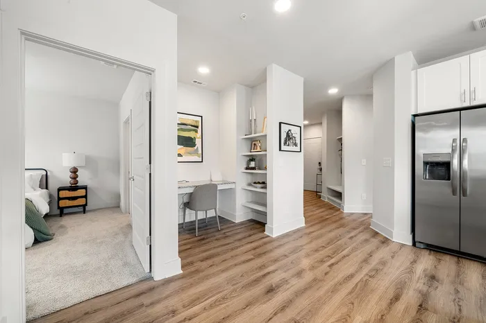 Modern apartment interior featuring sleek hardwood floors, a cozy bedroom entrance, stylish workspace, and contemporary stainless steel refrigerator.