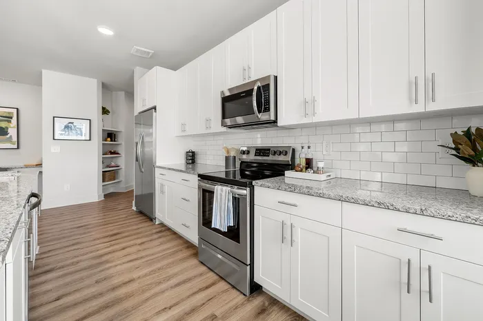 Modern kitchen with sleek white cabinetry, granite countertops, stainless steel appliances, and wood flooring, perfect for culinary creativity.