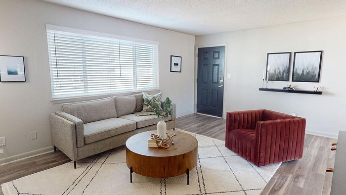 Inviting living room with modern decor, featuring a cozy gray sofa, stylish red armchair, and chic wooden coffee table on a light-patterned rug.