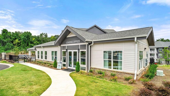 Inviting leasing office of a modern apartment complex, surrounded by lush greenery and a beautifully maintained lawn under a clear blue sky.