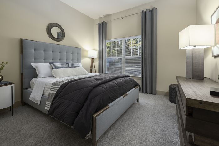 Inviting bedroom with a plush gray headboard, modern decor, and natural light pouring through large windows.