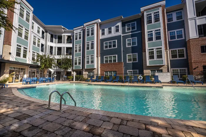 Luxurious apartment complex with a sparkling outdoor swimming pool surrounded by stylish lounge chairs, perfect for relaxation and leisure.