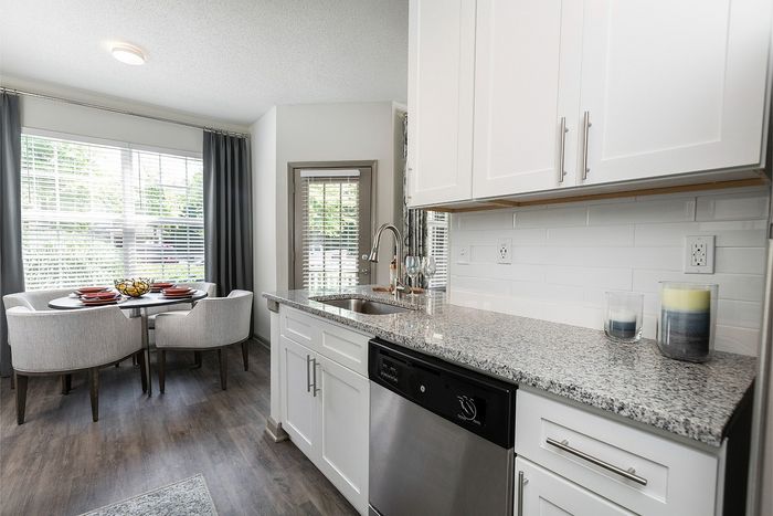 Bright and modern kitchen with sleek white cabinets and granite countertops, seamlessly leading to a cozy dining nook with stylish seating.