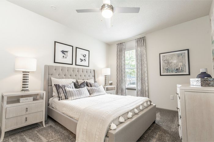 Bright and inviting bedroom with modern decor, featuring a plush bed, soft carpet, and large sunlit windows framed by elegant curtains.