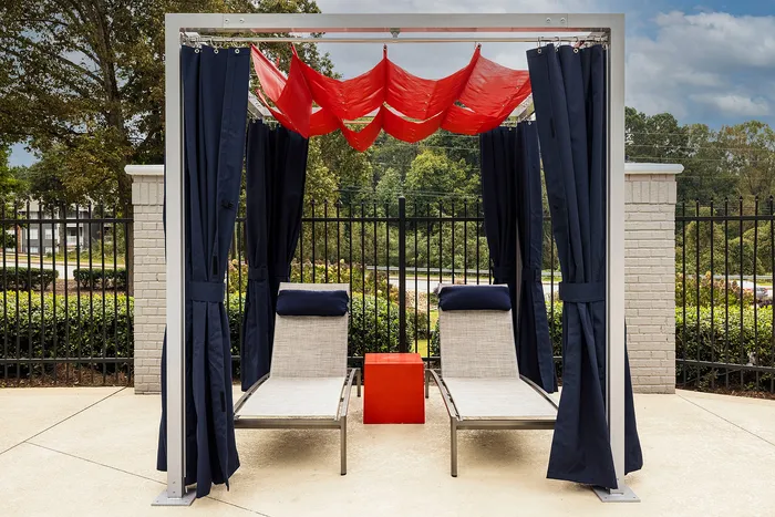 Inviting poolside relaxation area featuring stylish lounge chairs with bold red tables and umbrellas, perfect for a sunny escape.