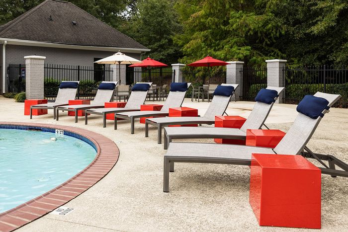Inviting poolside relaxation area featuring stylish lounge chairs with bold red tables and umbrellas, perfect for a sunny escape.