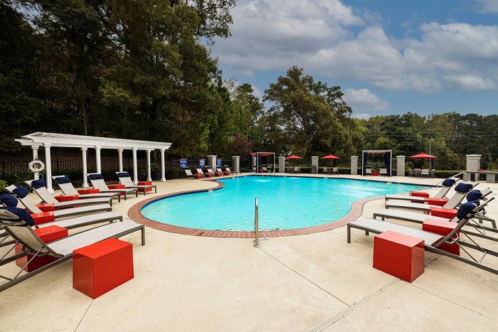 Inviting outdoor pool area surrounded by cozy lounge chairs and vibrant red accents, ideal for relaxation and featuring lush greenery on a sunny day.