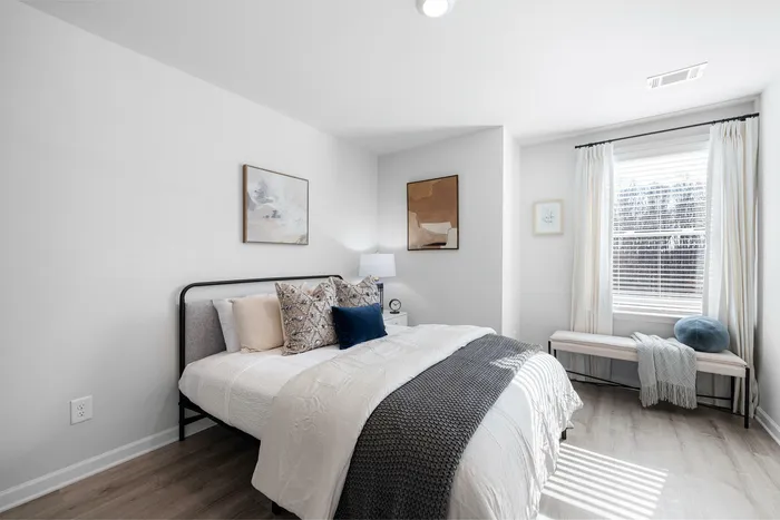 Inviting bedroom with stylish decor, featuring a cozy bed, plush pillows, and bright natural light from a large window.