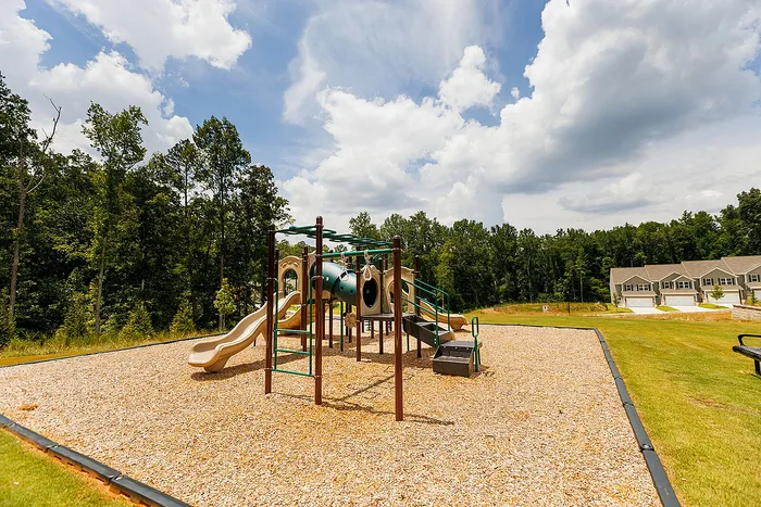 Inviting playground with modern slides and climbing frames, nestled in a scenic neighborhood surrounded by lush greenery and townhouse views.