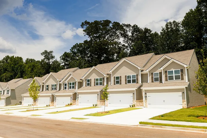 Modern row of townhouses with spacious driveways, nestled in a serene, lush green neighborhood.