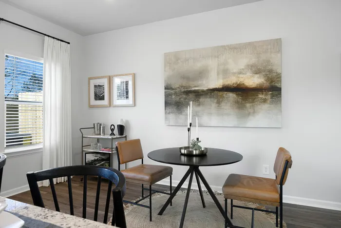 Elegant dining nook with modern art, round table, leather chairs, and natural light enhancing the cozy atmosphere.