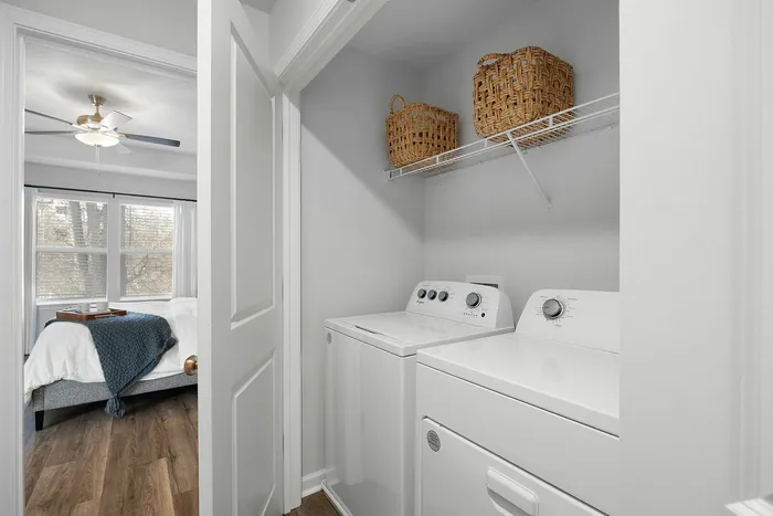 Bright laundry nook featuring modern washer and dryer, adjacent to a cozy bedroom with natural light streaming through large windows.