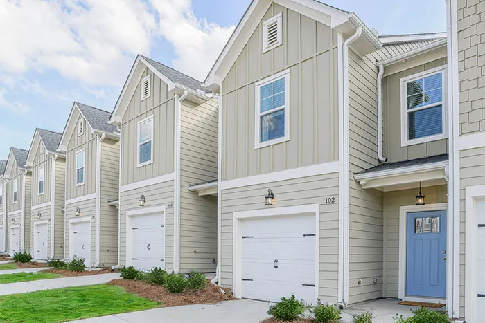 Charming row of modern townhouses with inviting blue doors, offering ample garage space and lush landscaping, perfect for contemporary living.