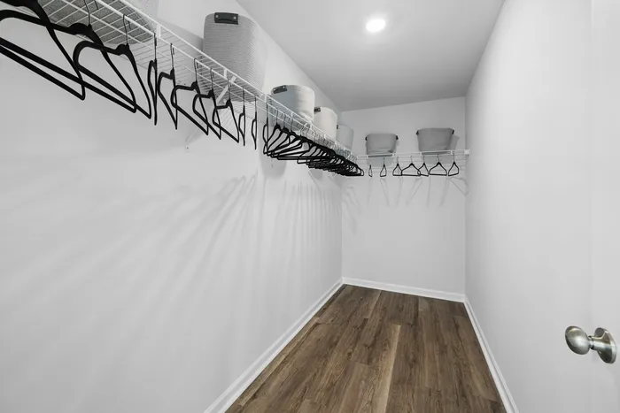 Spacious walk-in closet with sleek wooden flooring, ample shelving, and stylish storage baskets.
