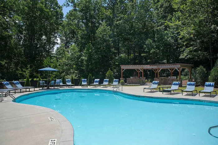 Luxurious outdoor pool surrounded by lush greenery, featuring stylish loungers and shaded seating area, perfect for relaxation.