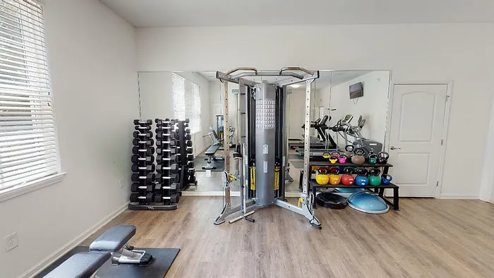 Modern fitness room equipped with weight machines, dumbbells, kettlebells, treadmills, and mirrored walls in a well-lit setting.