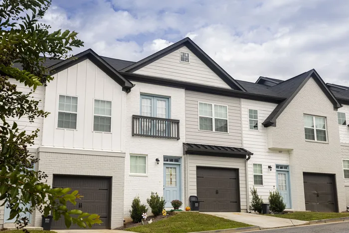 Charming row of modern townhouses with unique architectural accents and manicured landscaping under a bright, cloudy sky.