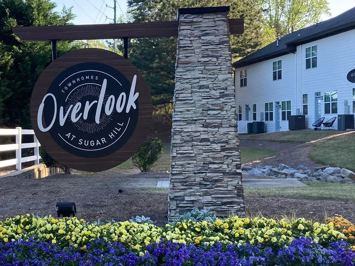 Charming entrance to Overlook at Sugar Hill townhomes, featuring vibrant flower beds and inviting signage near serene surroundings.
