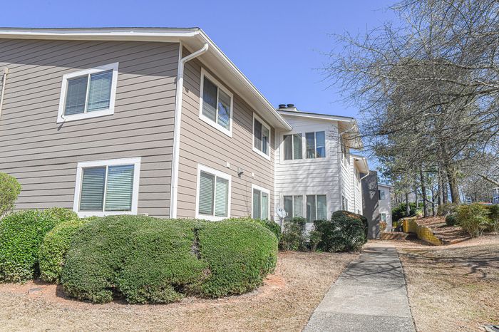 Charming apartment exterior with modern siding, lush green landscaping, and a sunny pathway in a vibrant community setting.