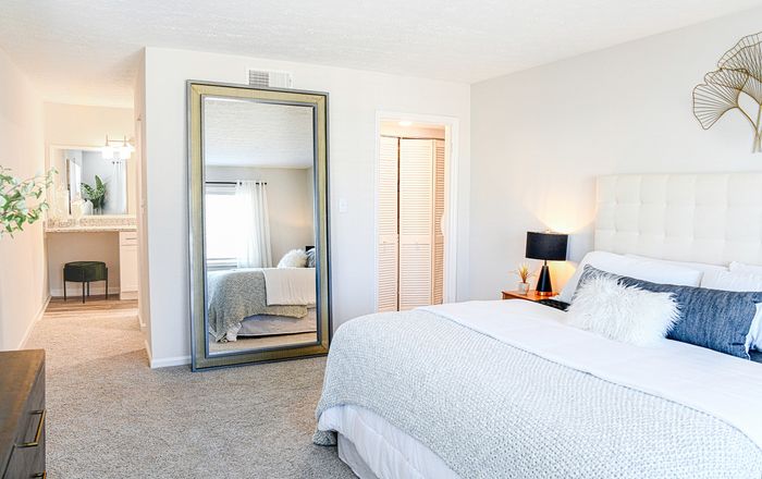 Luxurious bedroom with chic decor, plush bedding, and a large mirror reflecting natural light and warmth.