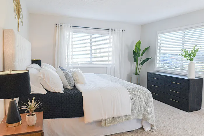 Bright and inviting bedroom with plush bedding, elegant decor, and ample natural light from large windows.