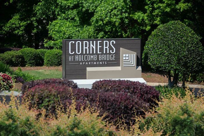 Welcoming entrance sign for Corners at Holcomb Bridge Apartments, surrounded by lush greenery.