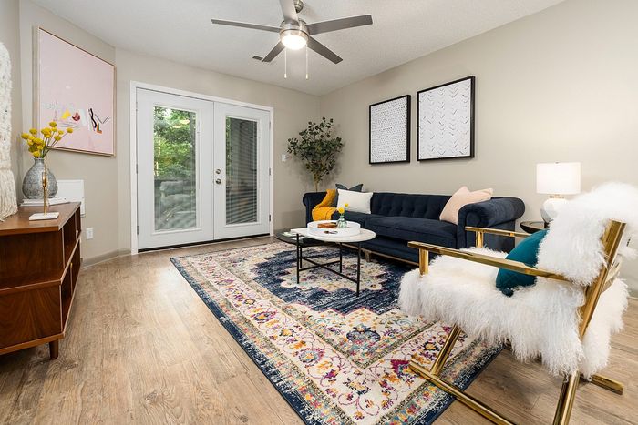 Chic living room with modern furnishings, vibrant rug, elegant decor, and large glass doors opening to greenery.