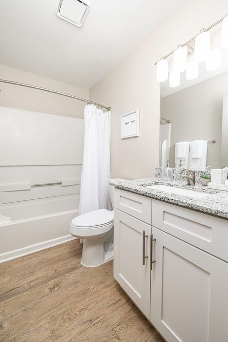 Modern bathroom featuring elegant granite countertop, sleek white cabinetry, and chic wooden flooring for a luxurious feel.