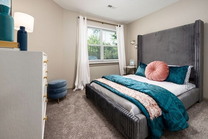 Chic bedroom with a plush gray bed, vibrant teal accents, and natural light from large windows, creating a serene retreat.