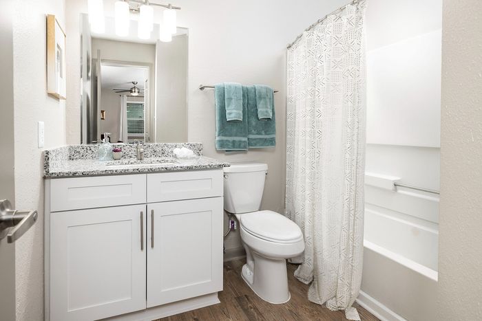 Bright and modern bathroom with granite countertop, stylish white cabinets, and elegant shower curtain, complemented by soft teal towels.