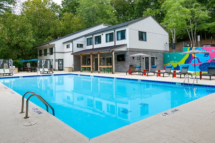 Inviting apartment community pool area with modern seating, vibrant mural, and lush trees in a serene setting.