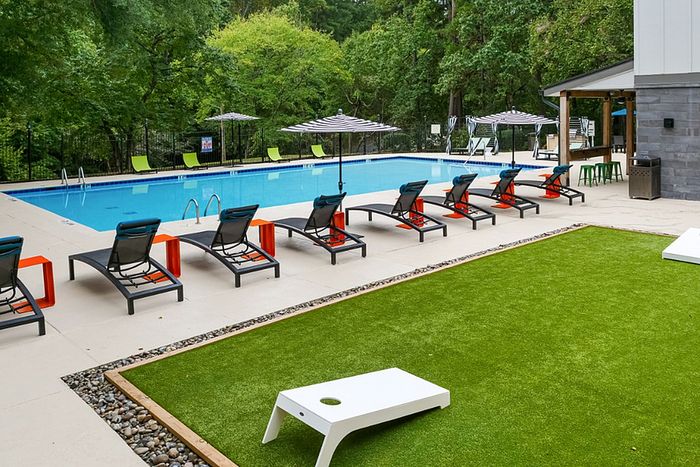 Luxurious outdoor pool area with sleek lounge chairs, vibrant umbrellas, and a lush green lawn for relaxation and leisure.