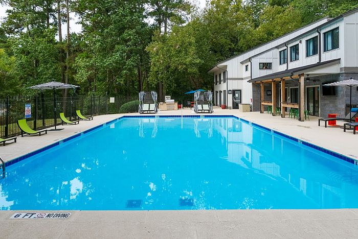 Inviting outdoor pool area with modern loungers, surrounded by lush greenery and a contemporary clubhouse.
