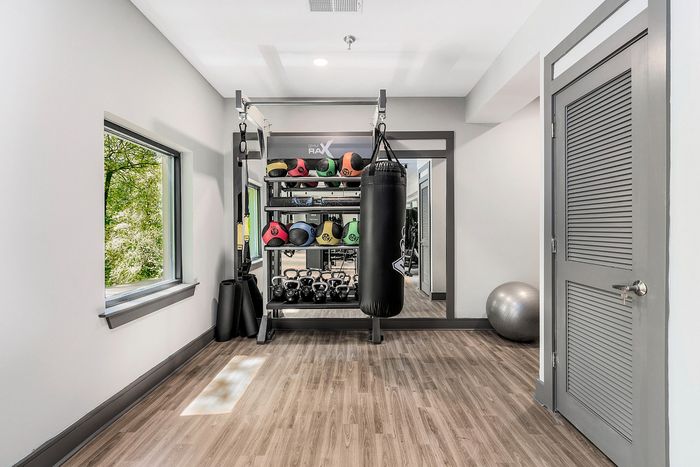 Modern fitness room with a variety of equipment including kettlebells, medicine balls, and a punching bag, set in a sleek interior with natural light.
