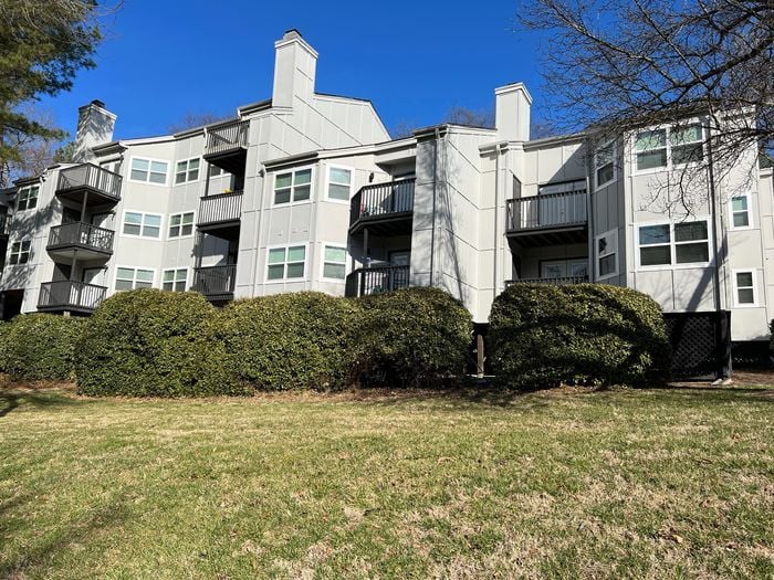 Attractive modern apartment building with private balconies, lush greenery, and a vibrant blue sky backdrop.